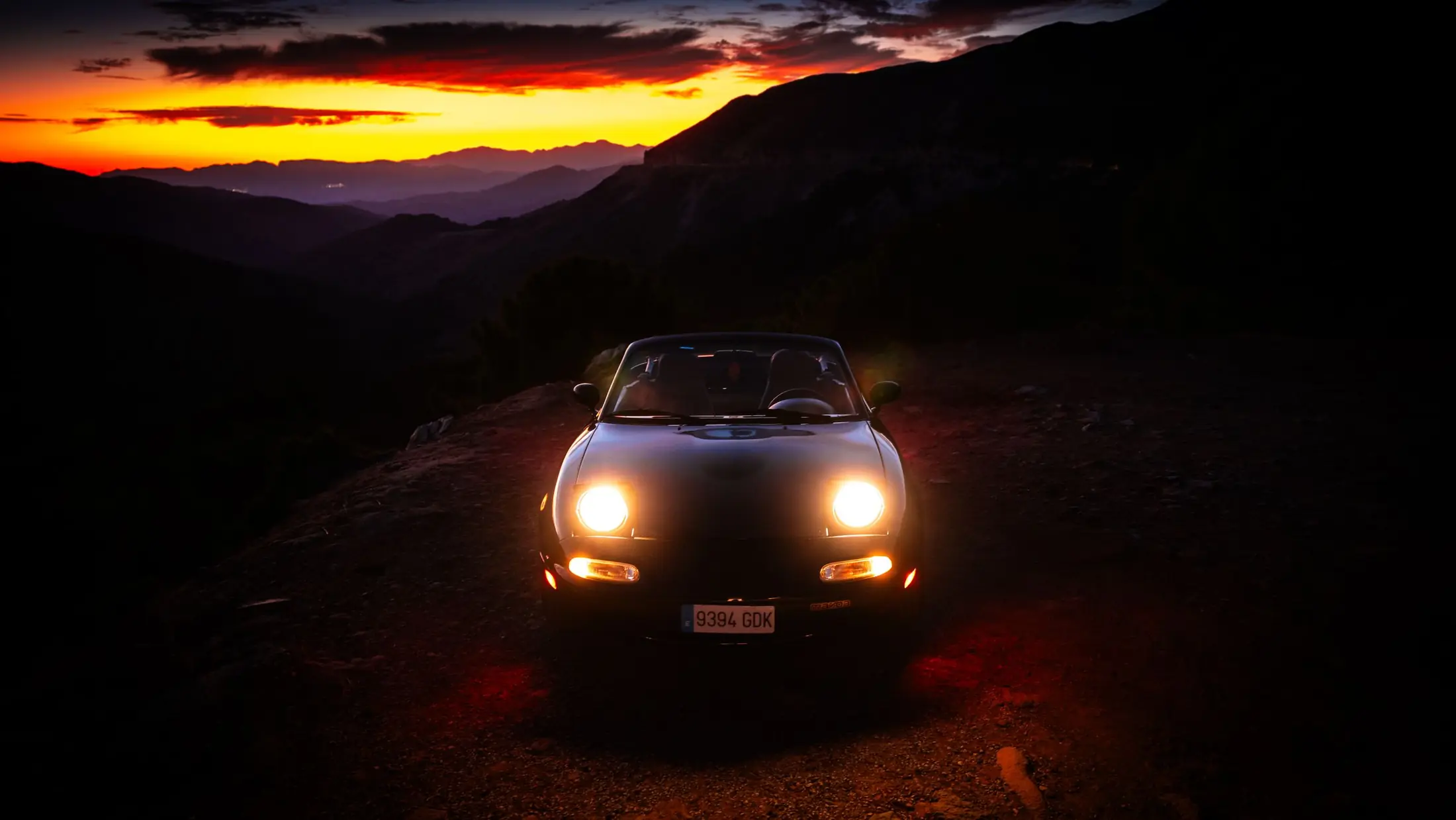 Voiture de sport phares allumés sur une route de montagne au crépuscule