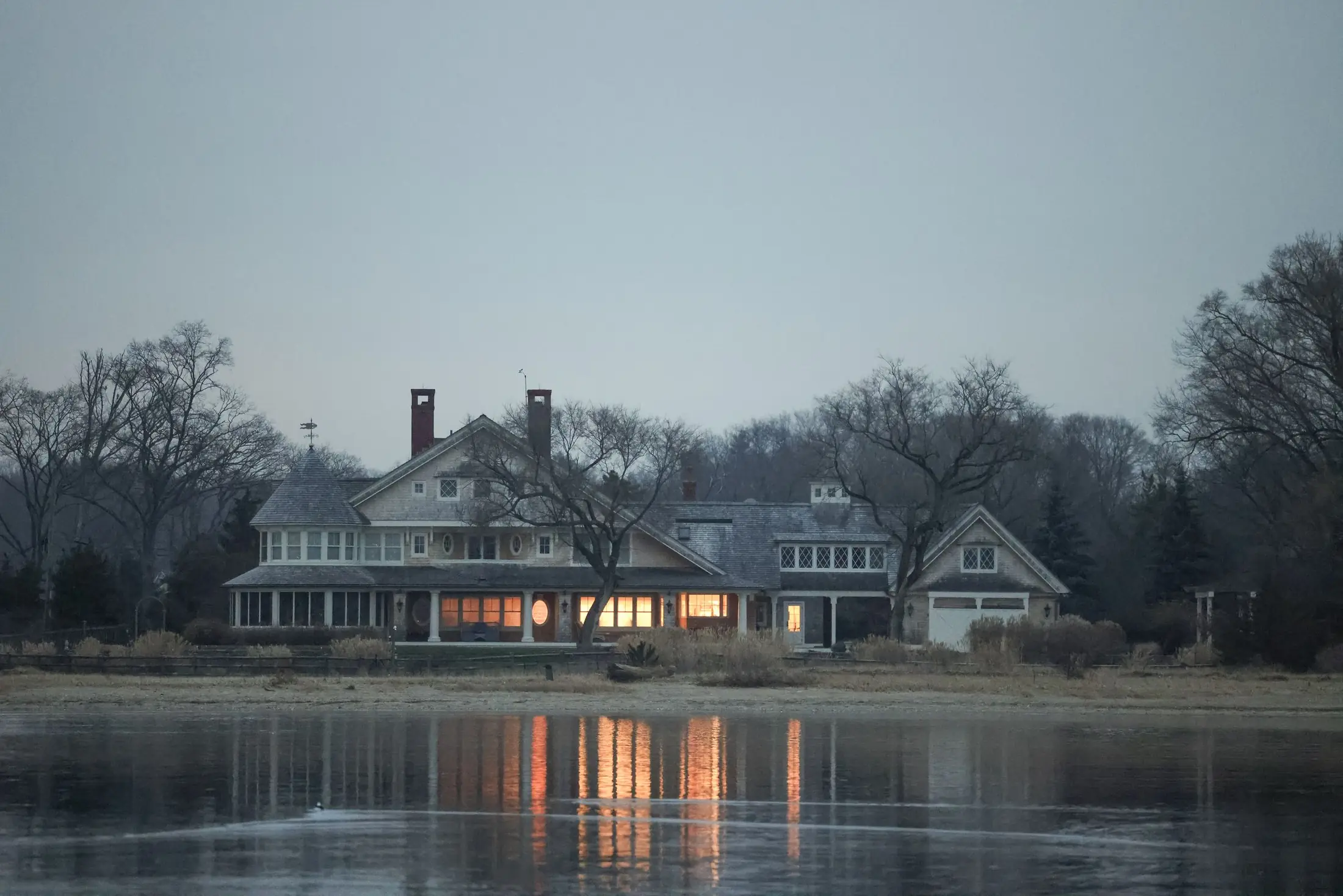 Maison au bord d'un lac, fenêtres éclairées à la tombée de la nuit